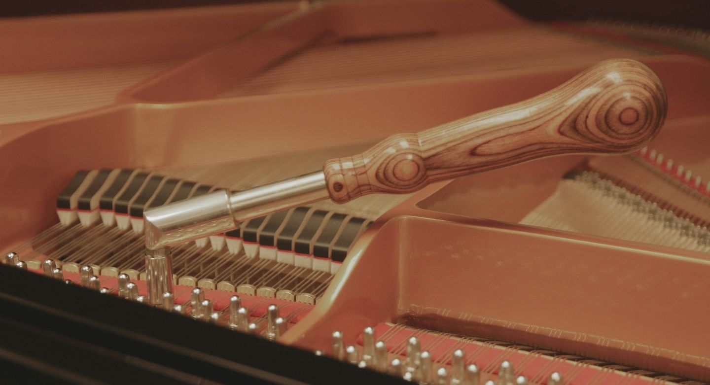 Detalle de las cuerdas y clavijas de un piano siendo afinado con herramientas de precisión